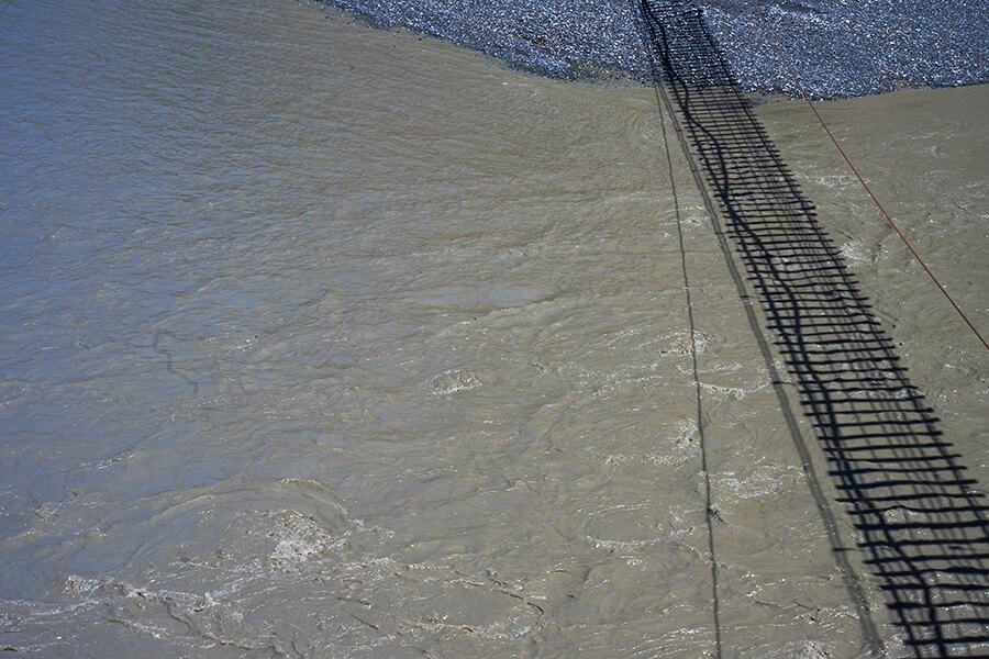 Shadow of a rope bridge over river water