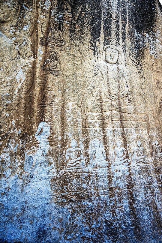 Weathered rock face with carved figures and blue wash
