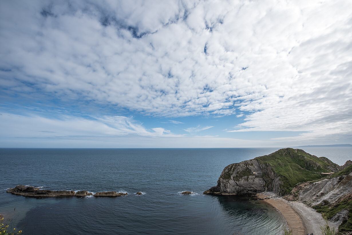 Wide cloudy sky over the sea and a green headland