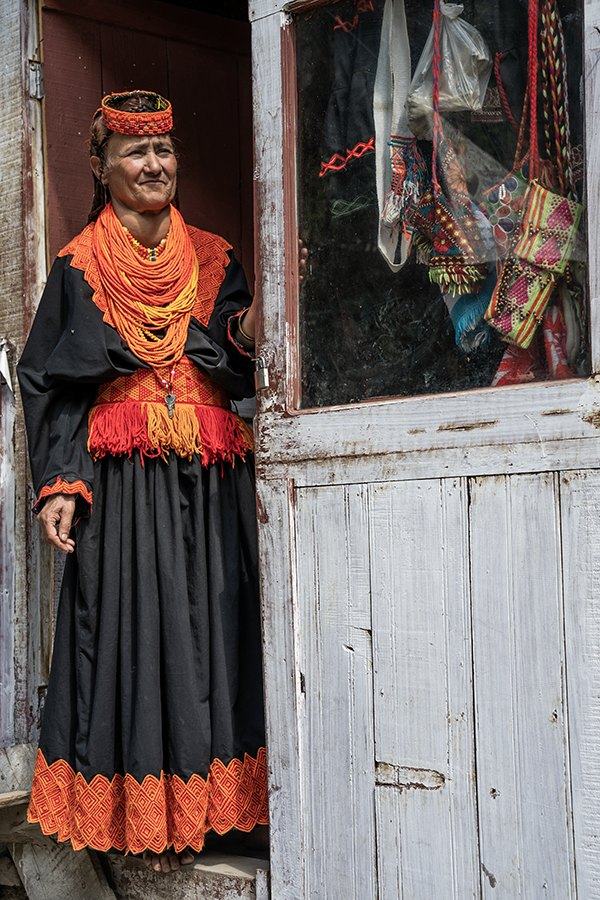 Woman in black and orange dress with layered orange necklaces standing in a doorway